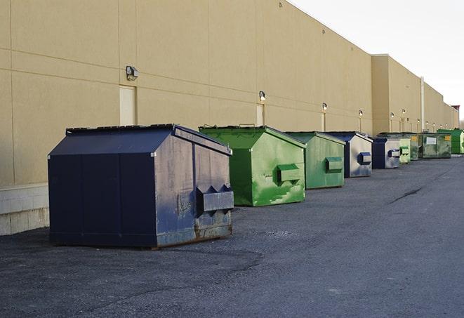 a construction worker unloading debris into a blue dumpster in Barton NY